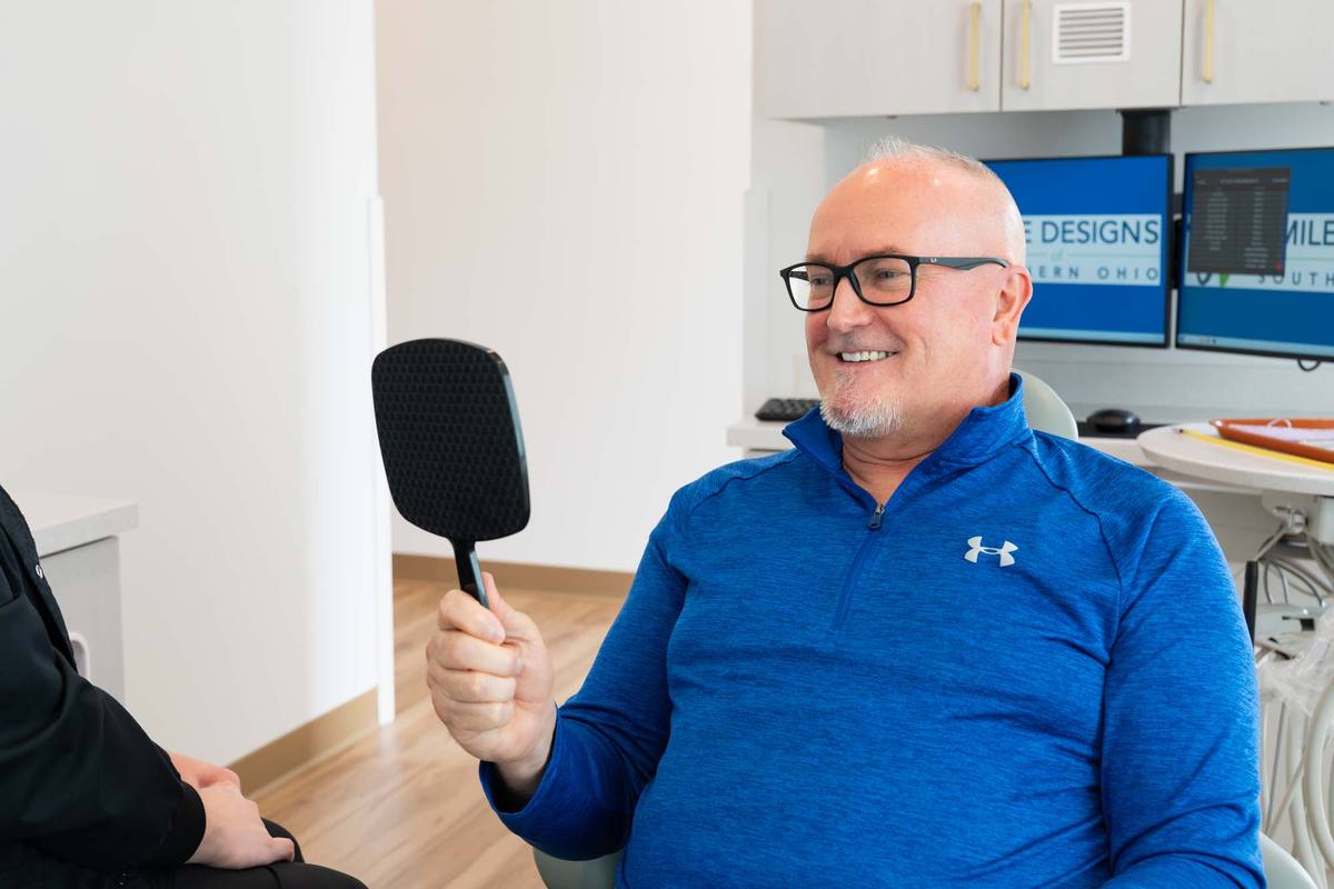 Smiling patient checking his teeth in a hand mirror