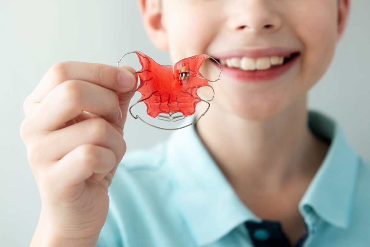 Smiling young patient holding a red retainer